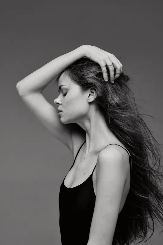Black and white portrait of a thoughtful woman with long hair in a sleeveless top, showing elegance and calm emotions.
