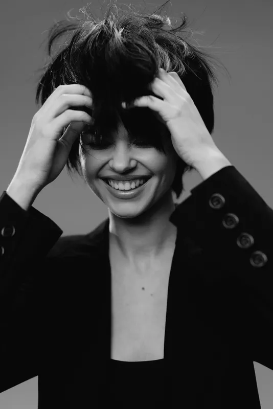 Smiling woman with tousled hair wearing black jacket in black and white portrait expressing joy and confidence.