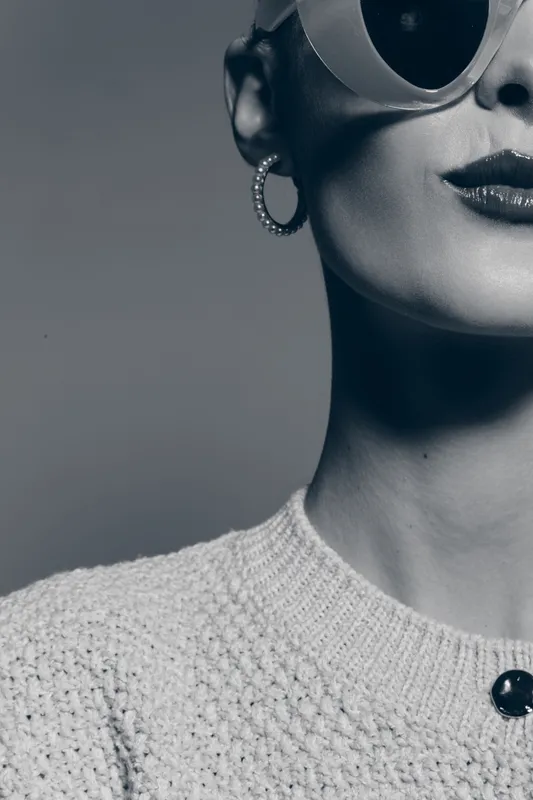 Close-up of a stylish caucasian woman with fair skin wearing round sunglasses and hoop earrings. She wears a textured sweater, minimalist and modern fashion concept.