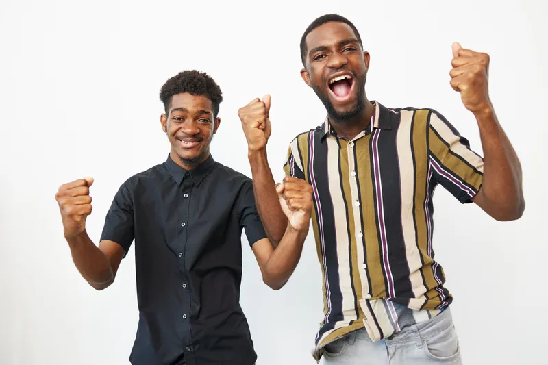 Two cheerful black men expressing excitement and joy, showcasing their vibrant personalities and stylish outfits. Perfect for conveying positivity and celebration.