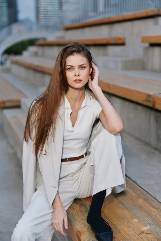 Professional woman in suit exuding confidence, seated gracefully on wooden steps, showcasing a modern business style with natural lighting and urban background.