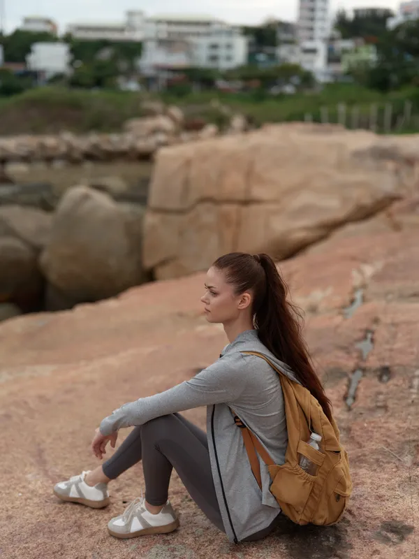 Young woman in casual sportswear enjoying a moment on rocky terrain by the coast, perfect for outdoor lifestyle and travel themes
