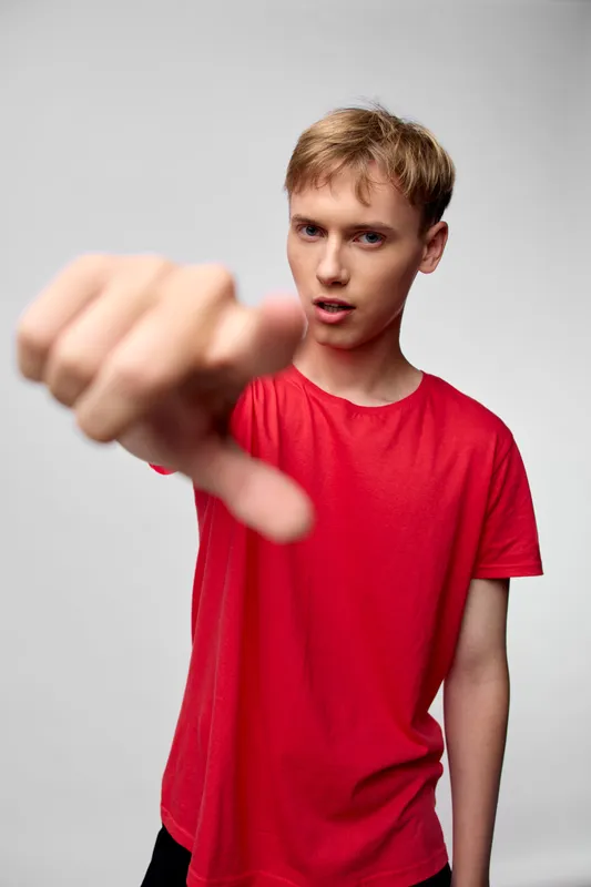 Disapproving man in a red shirt delivers a bold thumbs down gesture, signaling rejection or critique in a focused studio shot with intense expression and direct gaze