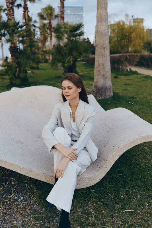 woman in white suit sitting outdoors with thoughtful expression business fashion concept urban park background