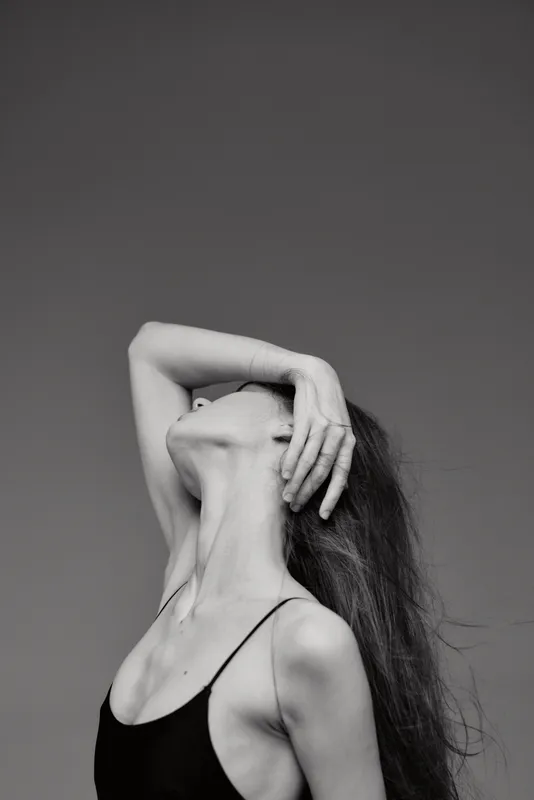 Black and white portrait of a woman with long hair posing with hand on head against a gray background.