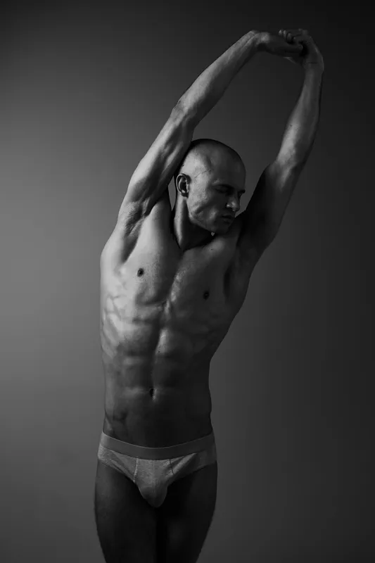 Athletic man stretching in a black and white image, showcasing muscular physique and dynamic pose, conveying strength and focus in fitness.