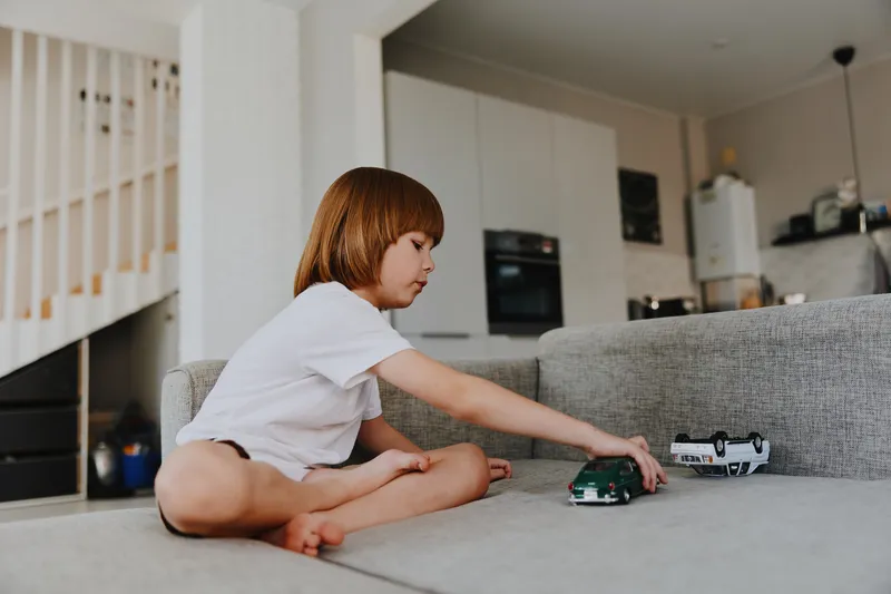 Young boy playing with toy cars indoors, showcasing creativity and joy in a cozy living room setting, emphasizing playtime and imagination.