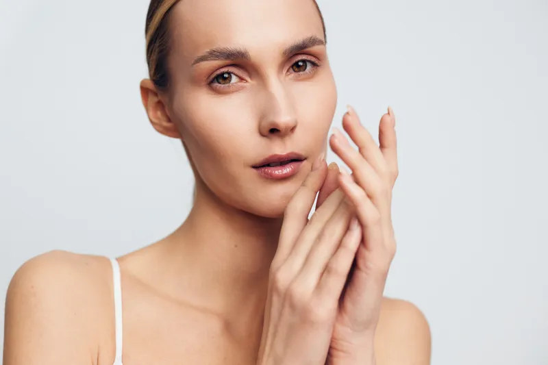 Closeup portrait of young woman with natural skin touching face with hands showing clean fresh complexion and calm expression isolated on light background