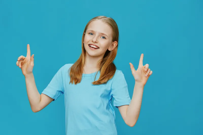 Happy young girl in a blue t shirt shows a cheerful gesture against a bright blue background, expressing joy and positivity
