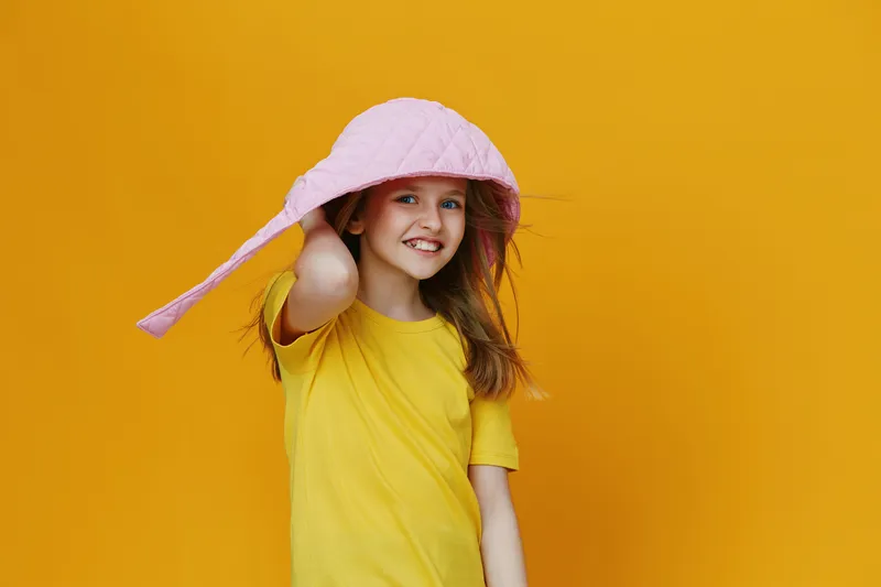 Cheerful girl wearing a yellow t shirt and pink hat against a vibrant yellow background, exuding joy and positivity, ideal for children s fashion and summer concepts