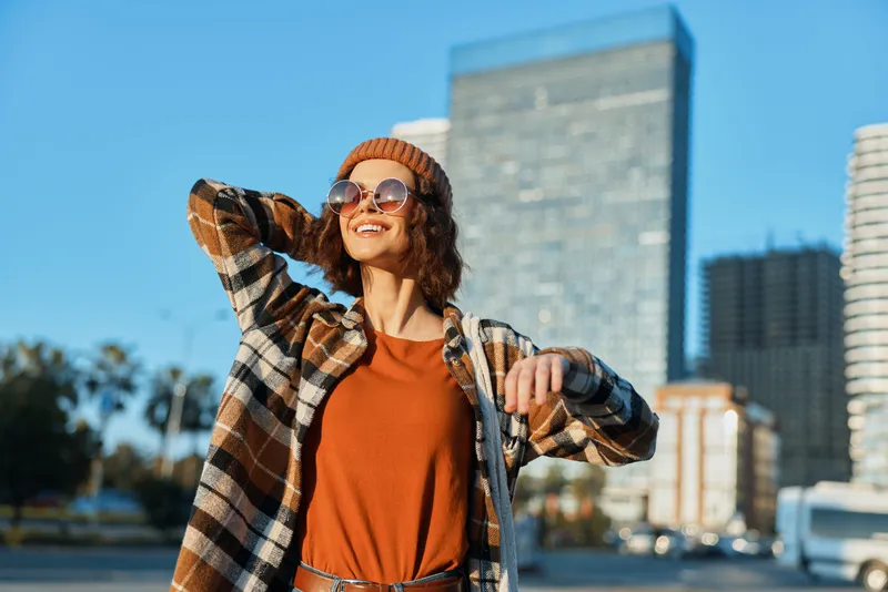 woman smile urban sunglasses beanie captured in a candid lifestyle portrait at golden hour glow, radiating authenticity, mindful living and emotional storytelling in modern city warmth.