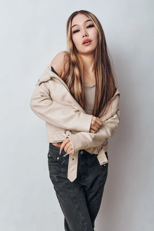 Young woman with long hair wearing beige jacket and black pants posing in studio on white background with casual confident expression and fashion style.
