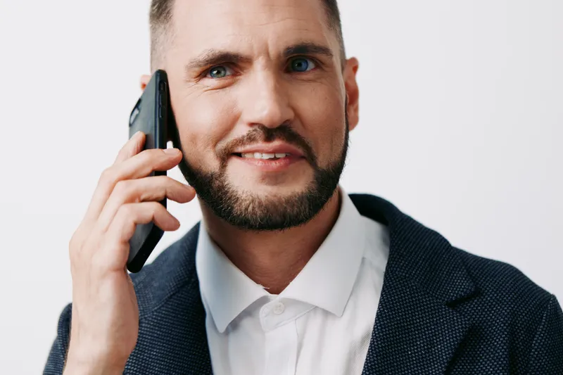 A professional businessman on a solid colored, isolated background communicates confidence and focus, captured during a phone call with a calm, composed expression and a poised posture.
