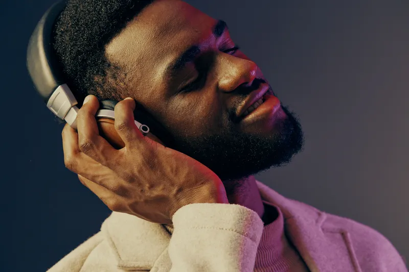 Young Black man enjoying music with headphones, expressing joy and relaxation, dressed in a beige sweater against a colorful background