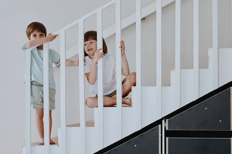Playful children exploring a white staircase, showcasing curiosity and joy. Their expressions capture the essence of childhood adventure and creativity.