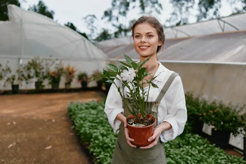 Young woman in a greenhouse holding a potted plant, showcasing joy and connection with nature, ideal for concepts like gardening and sustainability