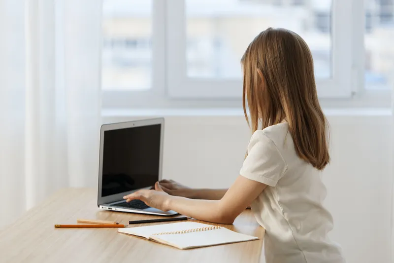 Young girl working on a laptop at a bright desk, focusing intently on her tasks while surrounded by a serene workspace, demonstrating productivity and concentration