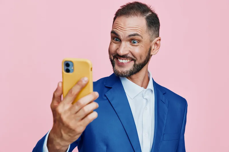 A confident business professional male takes a selfie against an isolated color background of pink, conveying enthusiasm and approachability in a modern corporate moment.