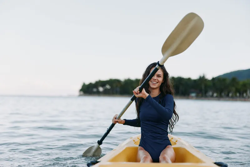 Smiling woman kayaking on calm water in nature, enjoying outdoor adventure and active lifestyle with paddle and blue outfit during daytime.