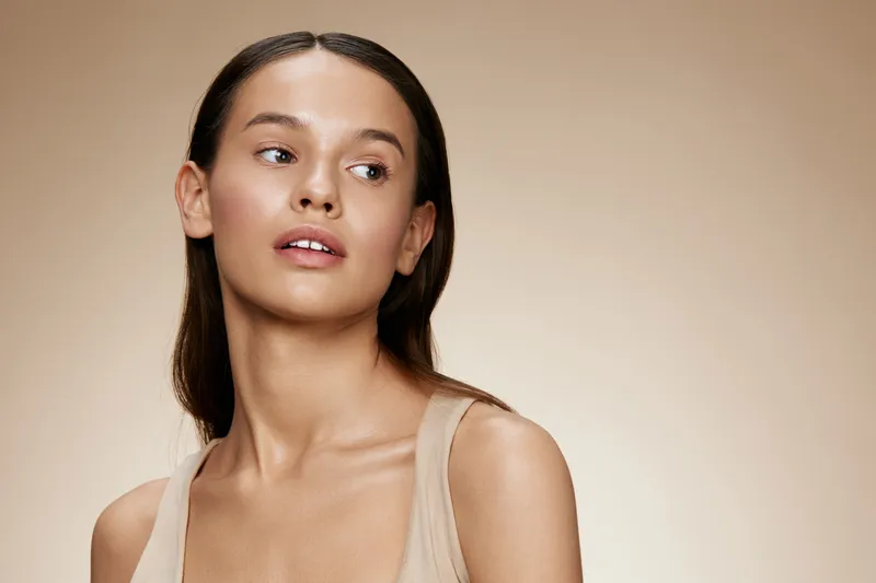 Young woman with natural beauty and soft makeup, showcasing healthy skincare and radiant skin amid a warm, neutral background