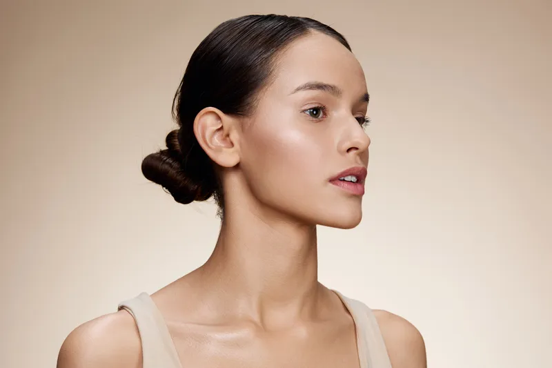 Beautiful woman with a natural makeup look against a warm beige background, showcasing healthy skin and minimalist fashion style