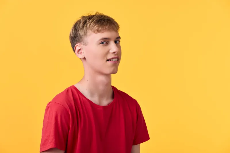 Clean studio shot of a young man in a red t shirt standing against a bright yellow background, conveying energy, optimism and casual style for fashion, lifestyle and stock photography.