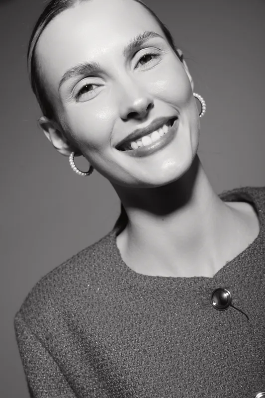 Smiling Caucasian woman with light skin and short hair wearing earrings and textured top in black and white portrait studio photo.
