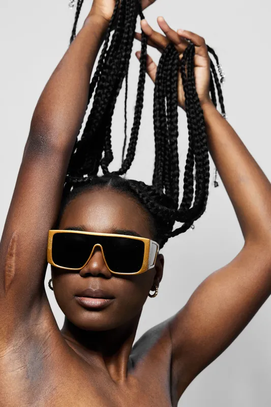Stylish model with braided hair and oversized sunglasses, showcasing confidence and modern fashion in a minimalistic studio background