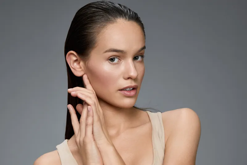 A beautiful young woman with smooth skin showcasing a natural beauty routine, highlighting healthy skin and hair in a minimalistic setting