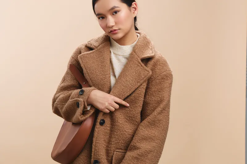 asian woman wearing a cozy wool coat stands against a neutral backdrop, exuding warmth and style with a calm, confident expression suitable for fashion and lifestyle photography.