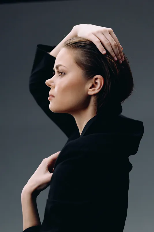 Profile of a thoughtful woman with dark hair wearing a black outfit against a dark background, showing calm and introspective mood.