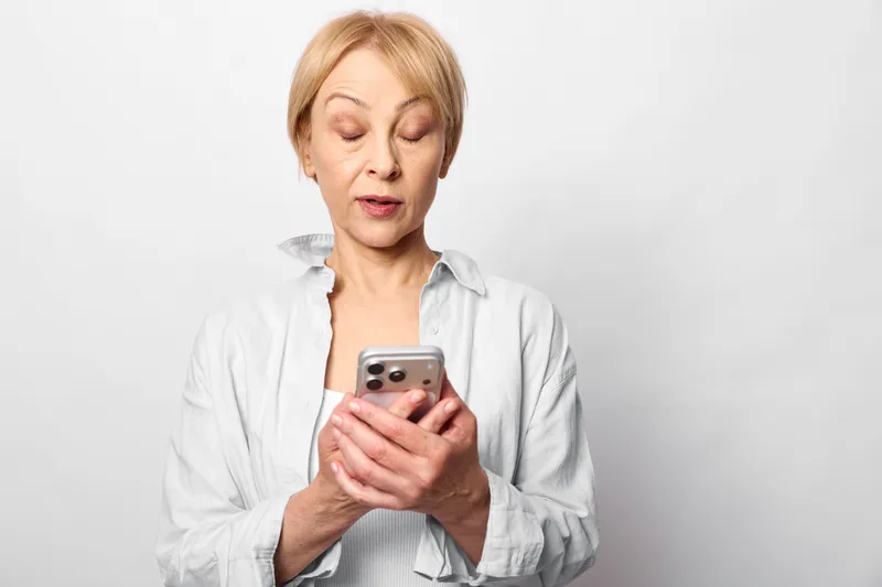 Woman holding smartphone, stress and anxiety shown, digital mobile screen moment, white studio background, communication and wellbeing concept, worried expression, soft studio light