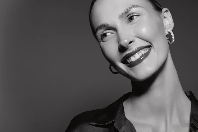 Smiling Caucasian woman with fair skin and dark lipstick looks away in black and white portrait. Concept for beauty, happiness, confidence, and makeup.