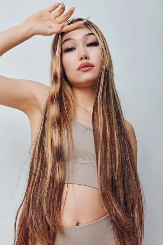 Young woman with long hair and natural makeup posing with hand above head wearing sleeveless top against plain background. Beauty, fashion and style portrait.
