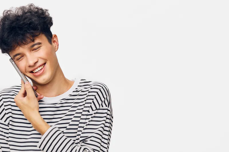 smiling man talking on smartphone, casual striped shirt, curly hair, happy expression, white background, communication concept