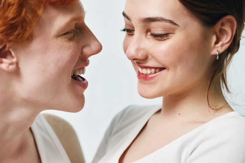 Couple smiling and looking at each other closely with happy expressions, emotional connection, and positive feelings in intimate moment on white background.