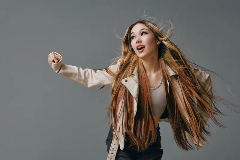 Woman with long hair dancing and moving energetically in casual clothes on gray background for lifestyle and motion concept.