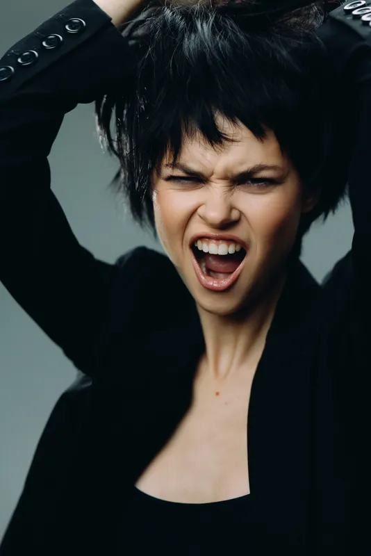expressive woman with short dark hair showing frustration wearing black jacket in studio lighting