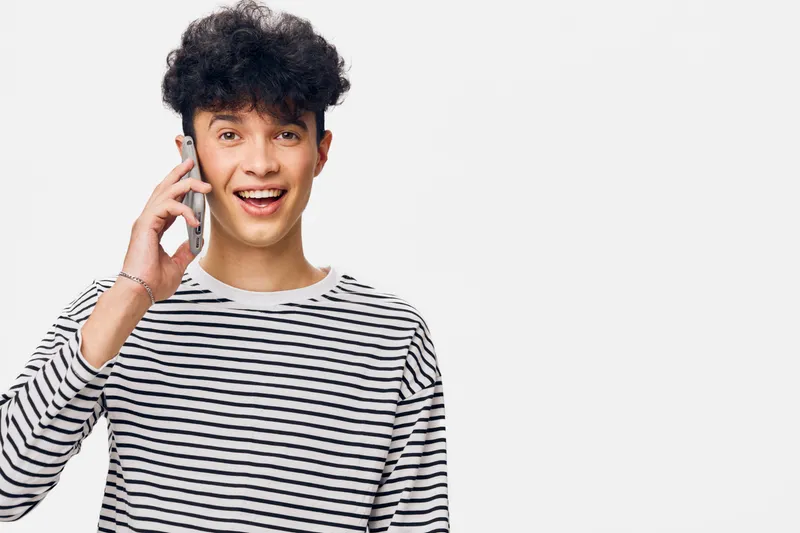 smiling man talking on smartphone wearing striped shirt with curly dark hair in studio with white background