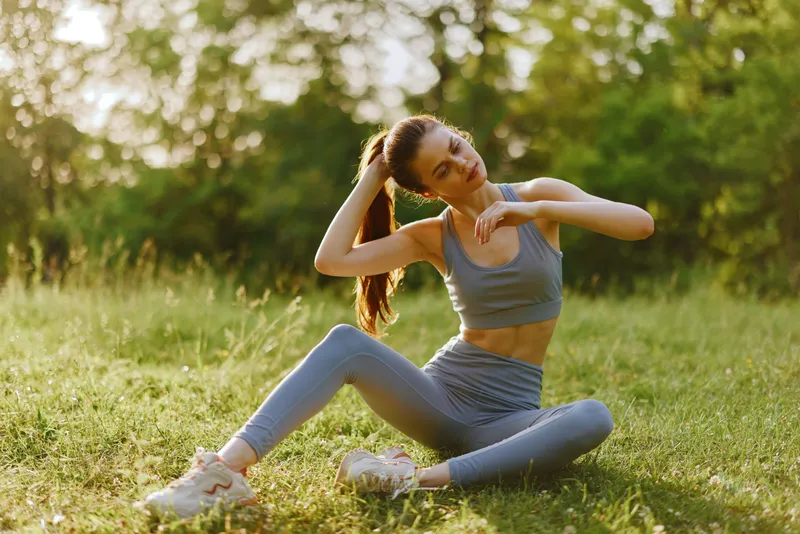 Young athletic woman stretching outdoors in a serene green park, wearing stylish activewear and exuding confidence and determination in a sunny setting