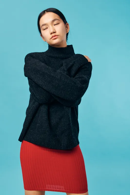 Young woman with eyes closed wearing black sweater and red skirt standing arms crossed on blue background for fashion portrait and casual style concept.