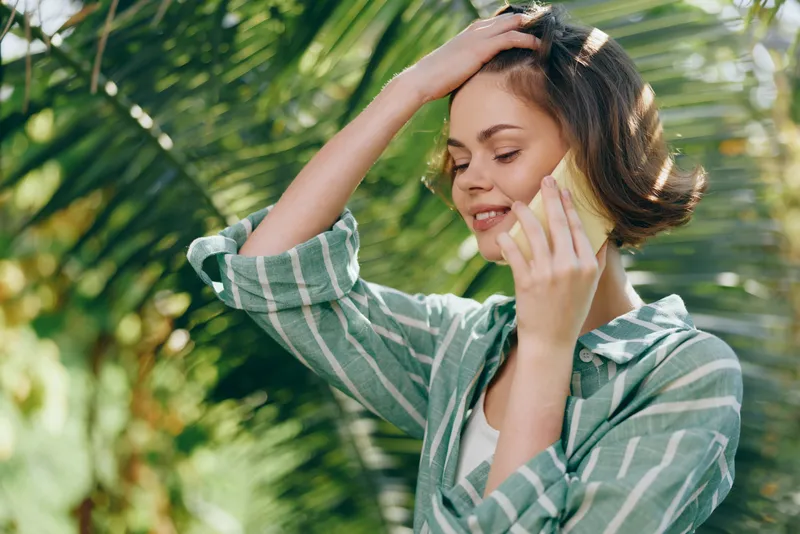 Portrait of a smiling woman outdoors in bright sunlight, wearing a striped green shirt, with wind in hair and a relaxed, natural pose.