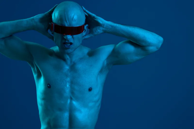 Dynamic man with futuristic glasses exhibiting intense emotions in a blue light setting, showcasing strength and determination in a captivating pose.