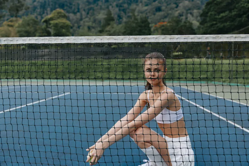 Young athletic woman in sportswear sitting by the tennis net, showcasing a confident and determined expression on a sunny day on the court