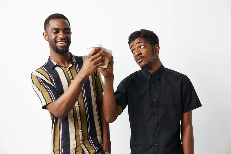 Two black men smiling and enjoying coffee together. Their joyful expressions and stylish outfits create a vibrant and engaging atmosphere.