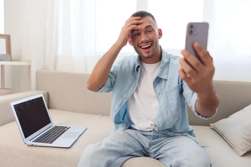Happy man enjoying a video call at home, embodying themes of men's mental health, emotional connections, and solo living choices in a cozy environment.
