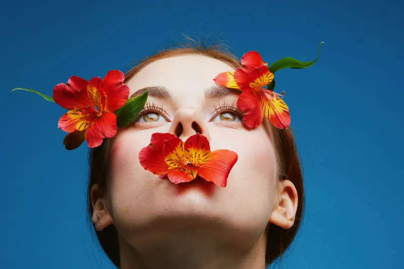 Close up of a beautiful woman with vibrant red flowers and a blue background, expressing emotions of tranquility and natural beauty in a fresh, seasonal vibe