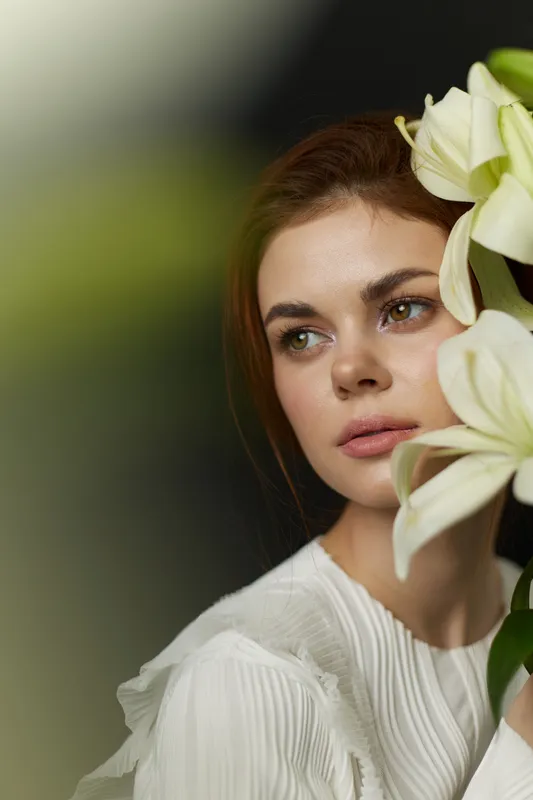 Young woman in a white dress holding white lilies, expressing tranquility and beauty against a soft green background, ideal for concepts of femininity and nature
