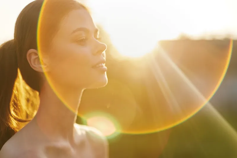Young woman with long hair enjoying sunlight outdoors, serene expression, highlighting beauty and nature s warmth during summer