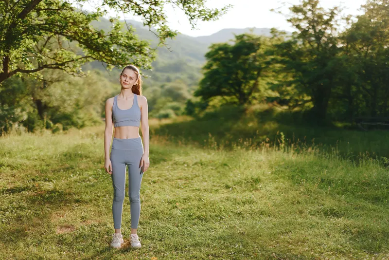 Young athletic woman demonstrating confidence in a serene outdoor setting, wearing sportswear, reflecting a healthy lifestyle and positive emotion